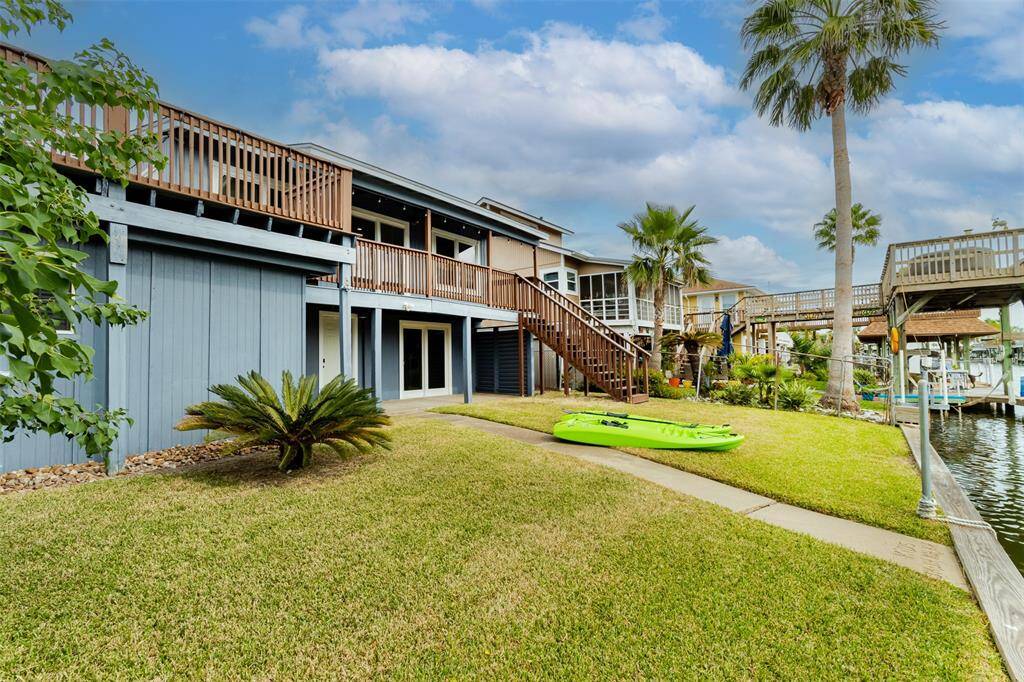This is a two-story waterfront home featuring a spacious lawn, a private dock, and upper-level balconies, set in a tranquil neighborhood with mature palm trees.