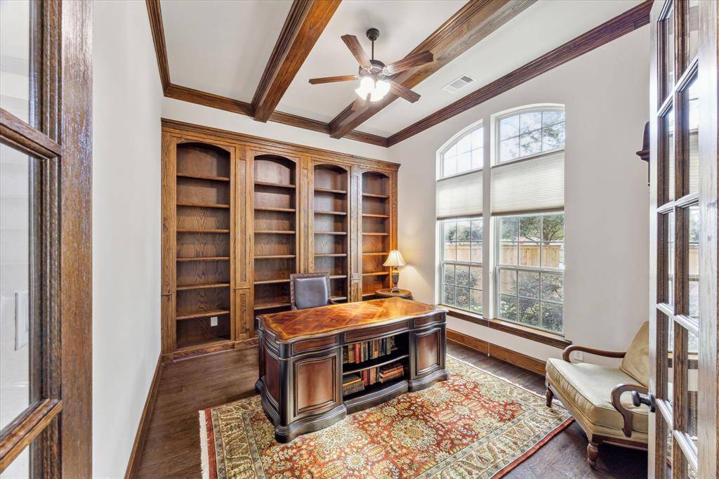 The study features stained trim, with beamed ceilings, crown moulding, and a wall of built-in bookshelves. You overlook the front yard and get excellent natural light. The furnishings here are available for sale. It's a very substantial, high-quality desk that was selected by a designer.