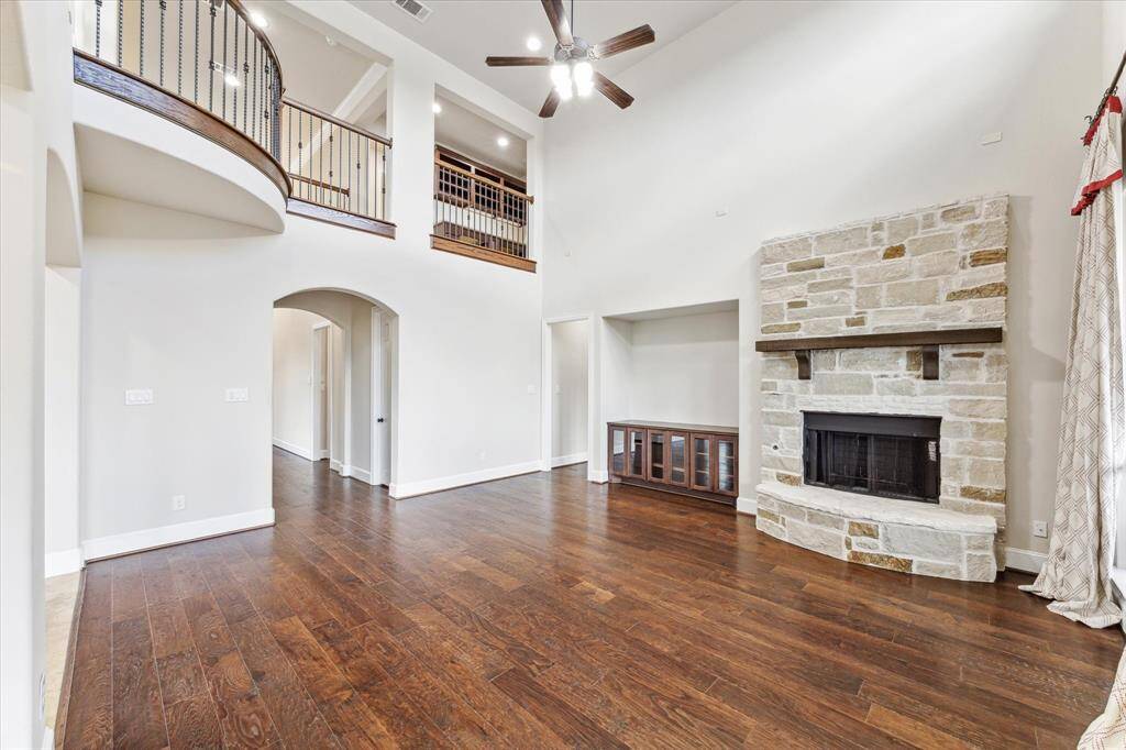 The two-story living room has soaring ceilings and lots of natural light. The stone fireplace is a focal point, and you have a base of built-in cabinetry for your TV. The wood floors are beautiful and the walls are neutral.