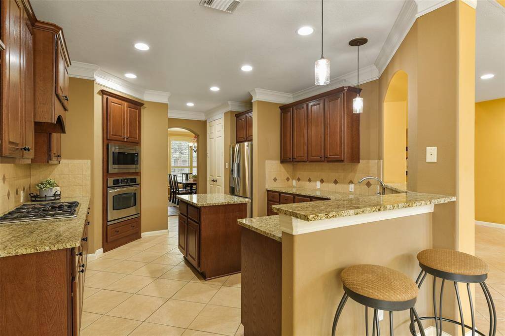 A raised breakfast bar wraps around the kitchen, providing additional seating and serving space when entertaining. Fine finishes in this kitchen include gleaming granite countertops, a neutral tile backsplash, recessed lighting, and stained wood cabinetry.