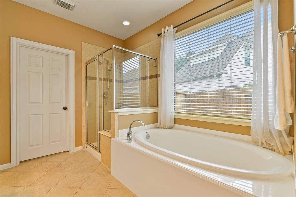 Relaxation awaits in this master bathroom that features a lengthy cultured marble vanity with a seated space with a lap drawer, dual basin sinks, white cabinetry, a framed mirror, a large garden tub, and a glass-enclosed shower with a tile surround.
