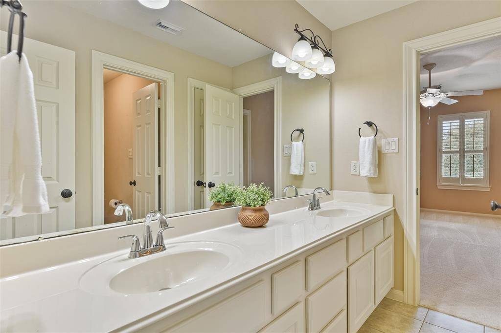 This Jack & Jill style bathroom services the previous bedroom and the next, offering a lengthy cultured marble countertop with dual basin sinks, abundant white cabinetry, tile floors, and a combined bathtub and shower with a tile surround.