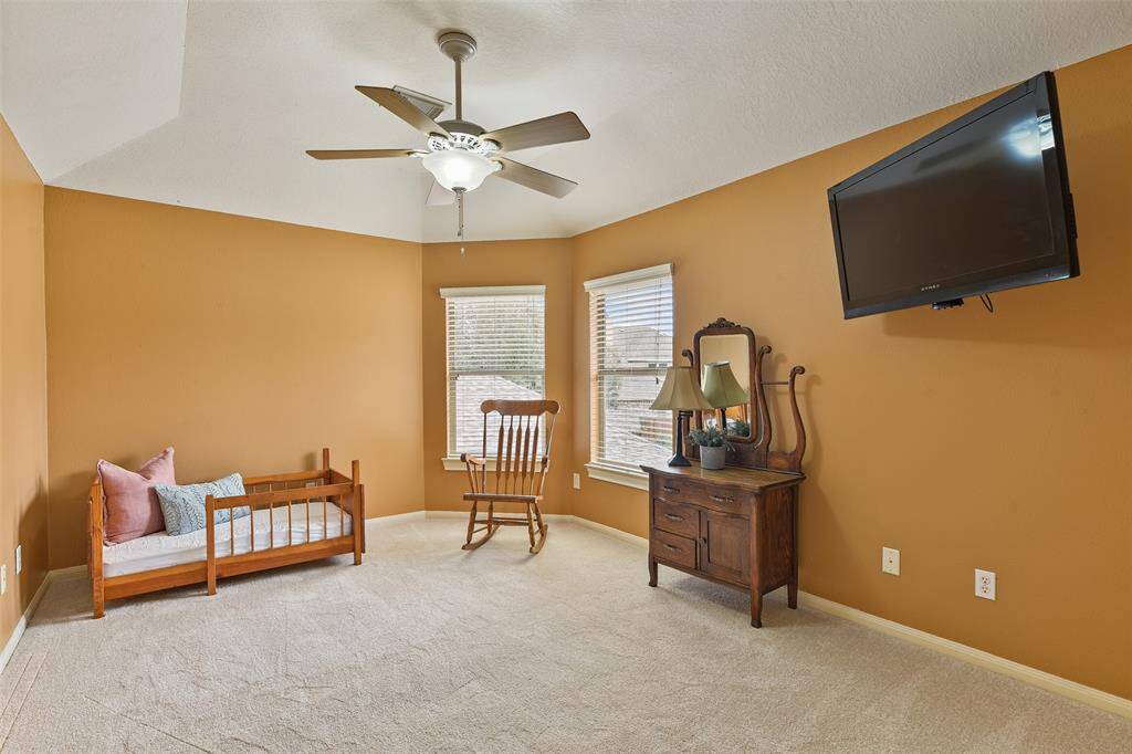 The fourth and final bedroom in this home features an elevated gambrel ceiling with a lighted ceiling fan, a neutral tan paint selection, walk-in closets, a pair of windows shaded by 2-inch blinds, and a bathroom just outside of the room.