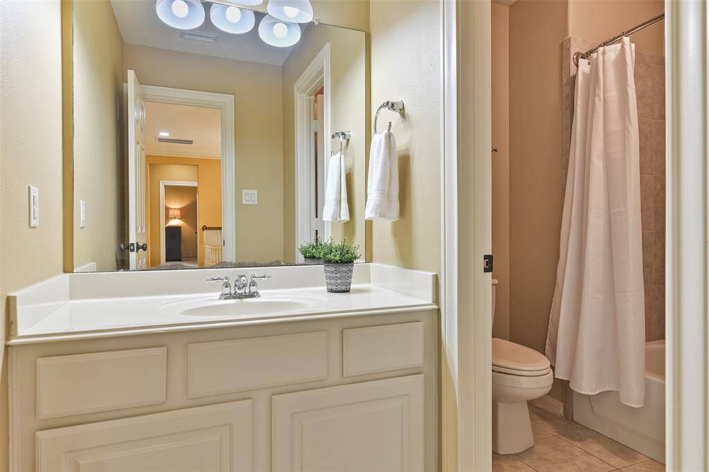 This bathroom is located just outside of the previous bedroom and it boasts a single cultured marble vanity with a basin sink, white cabinetry, tile floors, and a combination bathtub and shower with a tile surround.