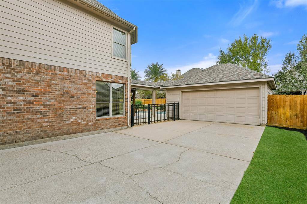 This home boasts ample parking space with a port cochere to a single garage plus a separate two-car garage and plenty of concrete parking or playing space in between, with an iron fence to the backyard area.