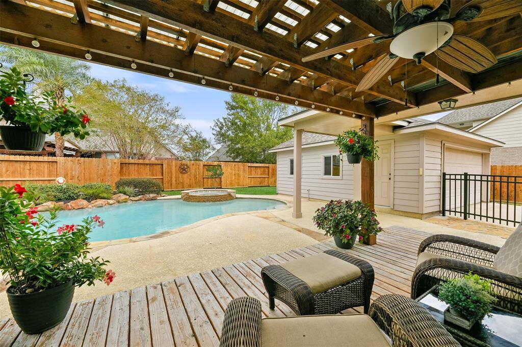 Step outdoors through the full-panel glass door in the breakfast room to this lovely 23'x10' covered patio area with a lighted ceiling fan, deck flooring, string lights, mounted speakers, and tranquil views of the private backyard paradise.