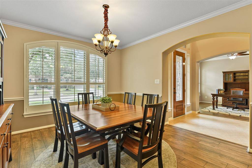 On the opposite side of the foyer, opposite the study, this inviting formal dining room features a 5 light scrolled iron chandelier, wood-look laminate floors, neutral paint trimmed with crown molding, and an expansive palladium arched window shaded by plantation shutters.