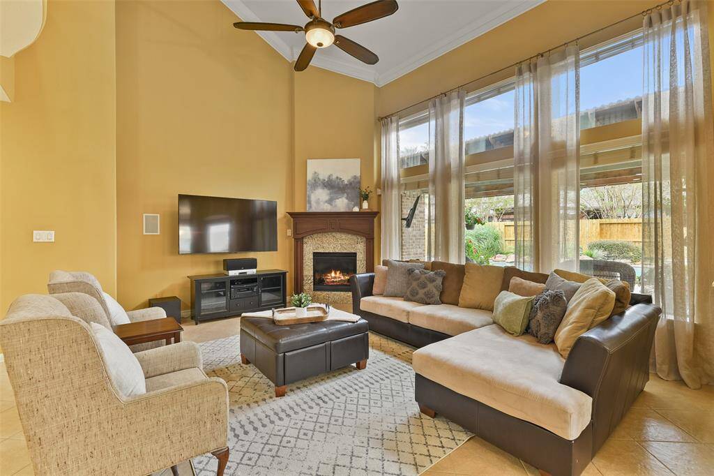 The family room is anchored by a beautiful corner-set gas log fireplace with a tile surround and a handsome stained wood mantle. Wall-to-wall windows with sheer draperies along the rear wall frame picturesque views of the backyard oasis.