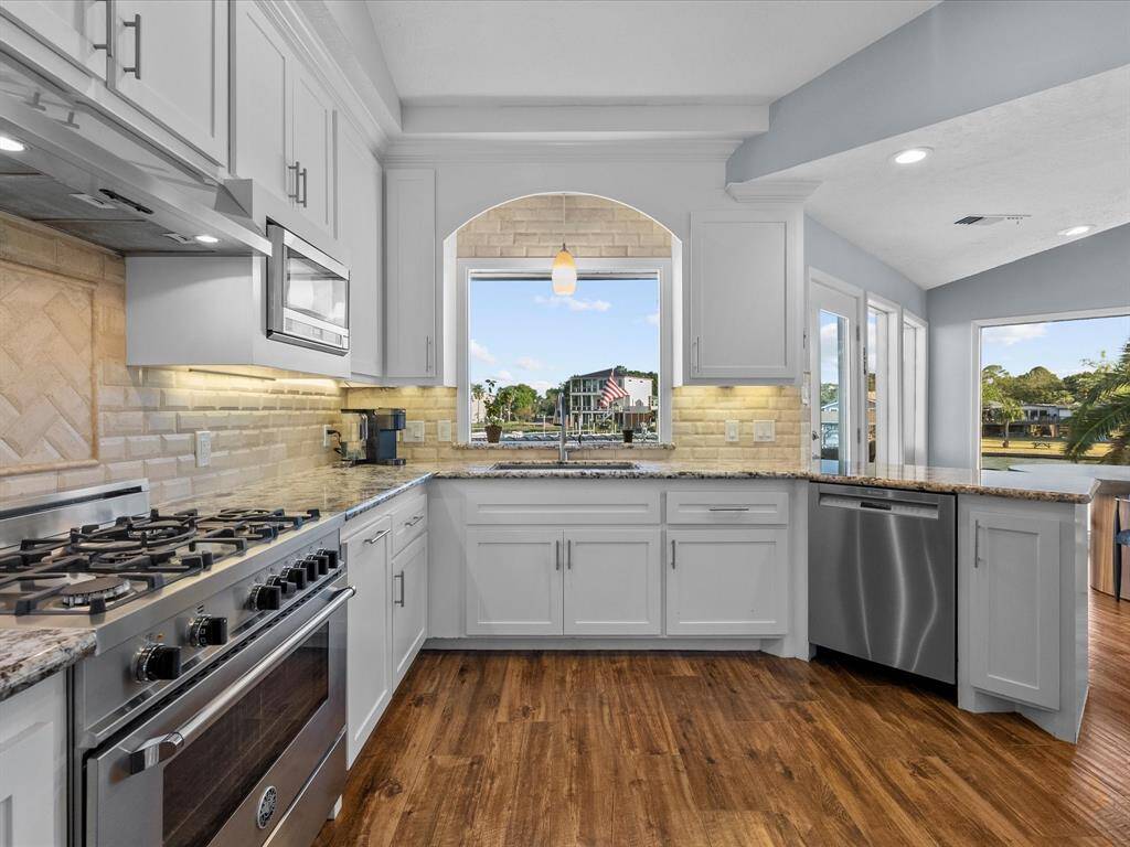 Spacious Kitchen with Stainless Steel Appliances and White Cabinetry, Complemented by Granite Countertops and Unbelievable Views of the Waterfront!