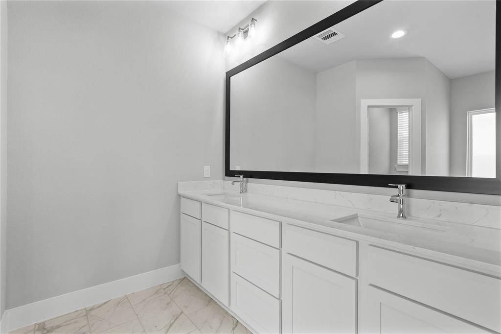 This primary bathroom is definitely move-in ready! Featuring stained cabinets with light countertops with dual vanities, framed mirror, spacious walk-in closet with shelving, high ceilings, custom paint, and sleek modern finishes.