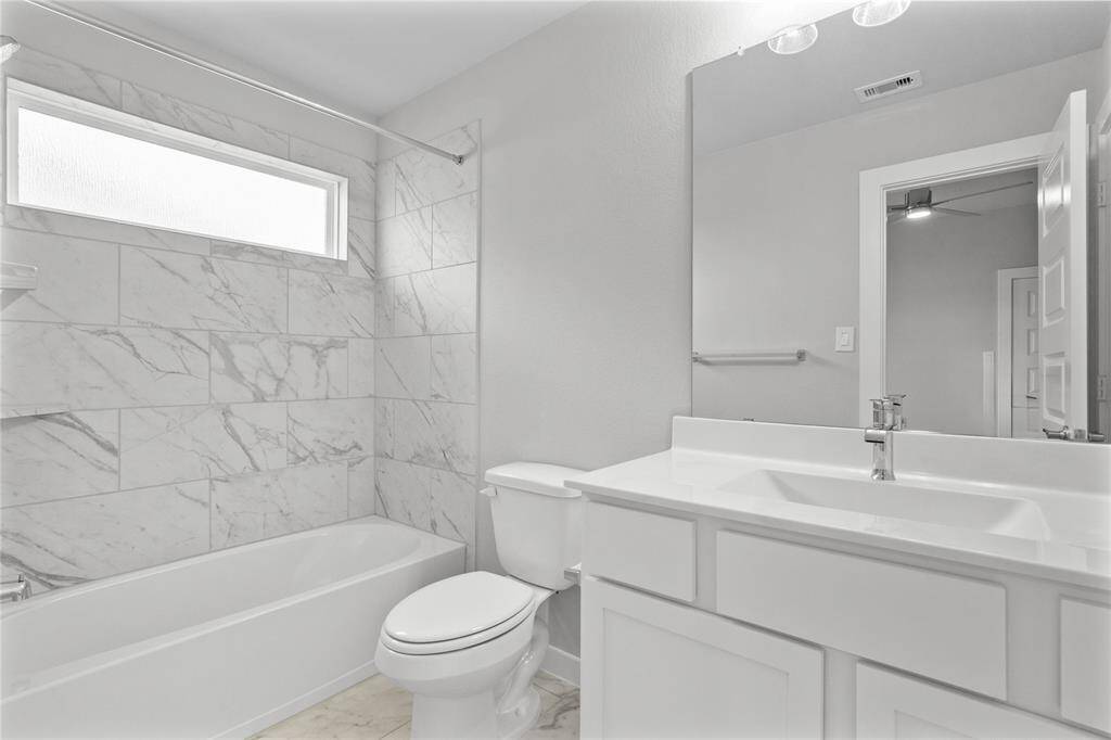 Secondary bath features tile flooring, bath/shower combo with tile surround, wood stained cabinets, beautiful light countertops, mirror, dark, sleek fixtures and modern finishes!
