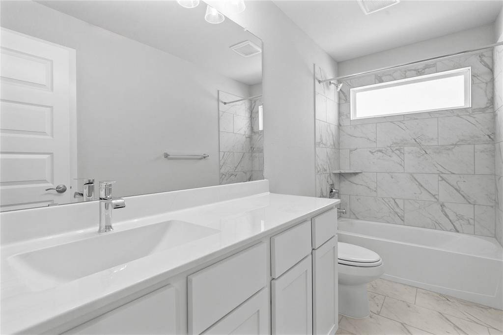 Secondary bath features tile flooring, bath/shower combo with tile surround, wood stained cabinets, beautiful light countertops, mirror, dark, sleek fixtures and modern finishes!