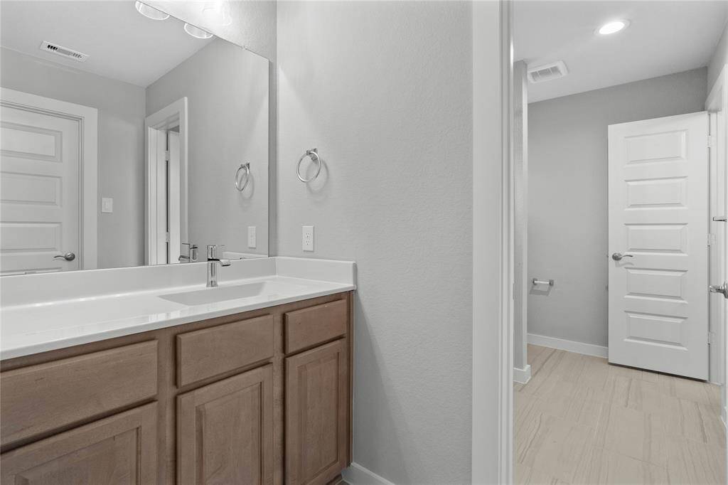 Secondary bath features tile flooring, bath/shower combo with tile surround, stained wood cabinets, beautiful light countertops, mirror, dark, sleek fixtures and modern finishes.