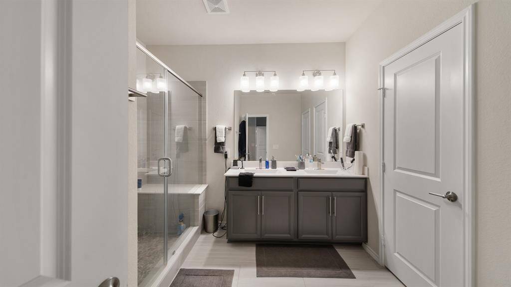 The primary bathroom features dual sinks and a walk-in shower with tile surround, glass door, and sitting area.