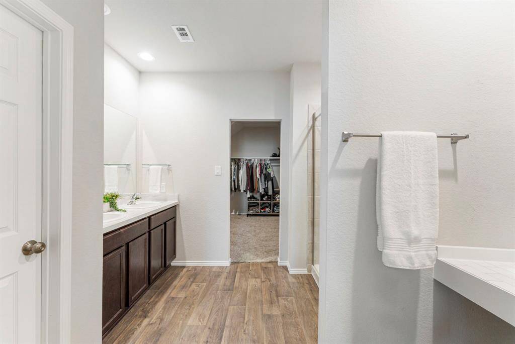 A very spacious and functional primary bathroom featuring a custom vanity, double sinks, a new glass shower door, and a bathroom door for added privacy.