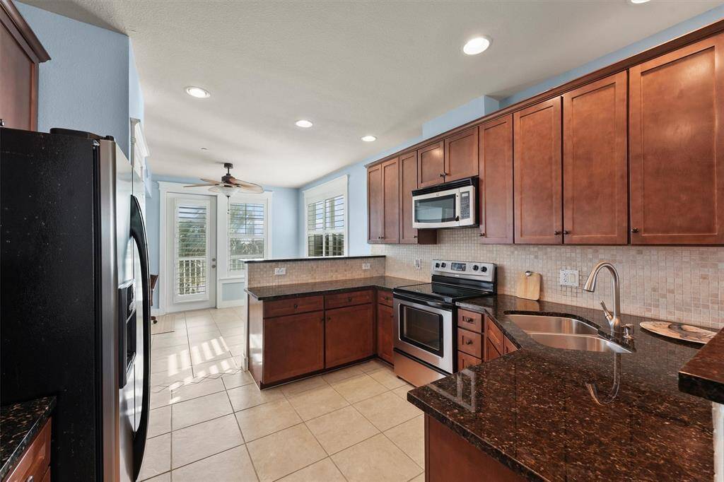 Natural light floods this beautiful kitchen through large windows, highlighting the sleek granite surfaces and classic tile backsplash. The open breakfast bar makes it easy to stay connected with guests in the living areas.
