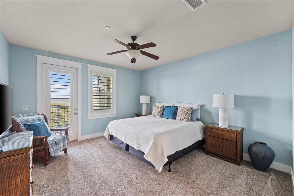 The spacious primary bedroom features serene blue walls and plush carpeting, creating a calm retreat. French doors and large windows bring in abundant natural light and lead to the balcony with sweeping views.