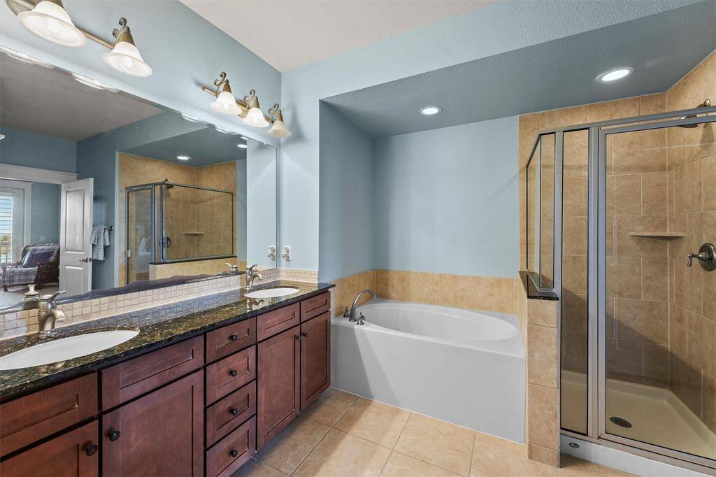 The attached primary bathroom offers dual sinks with a granite countertop and rich wood cabinetry, combining style and function for a refreshing daily routine.