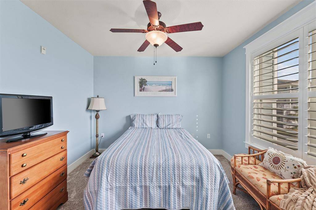 The guest bedroom is thoughtfully designed for comfort with a plush bed, ceiling fan, and charming wicker bench by the window—a perfect spot to unwind and take in the views.