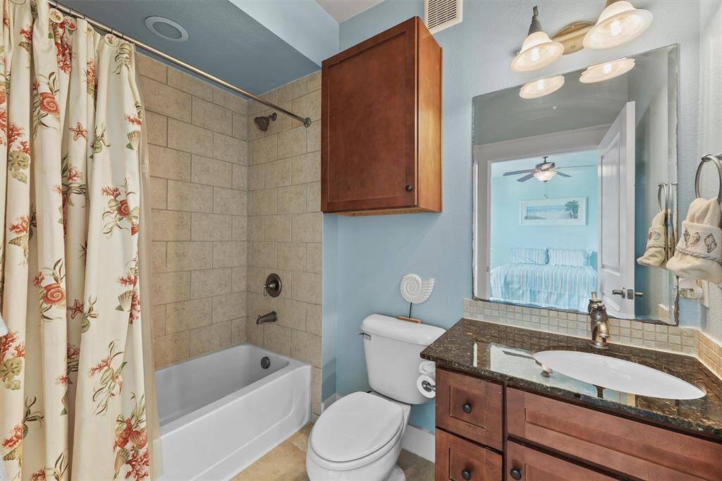 The guest en-suite bathroom features a tiled shower-tub combination, a vanity with granite countertop, and warm cabinetry, providing both style and convenience for visitors.