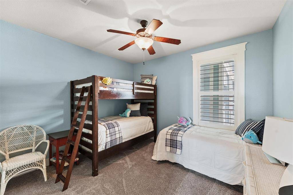 This cozy bedroom features a bunk bed alongside a single twin bed, creating a welcoming space for kids or guests. Soft blue walls and a ceiling fan add to the room's airy ambiance.