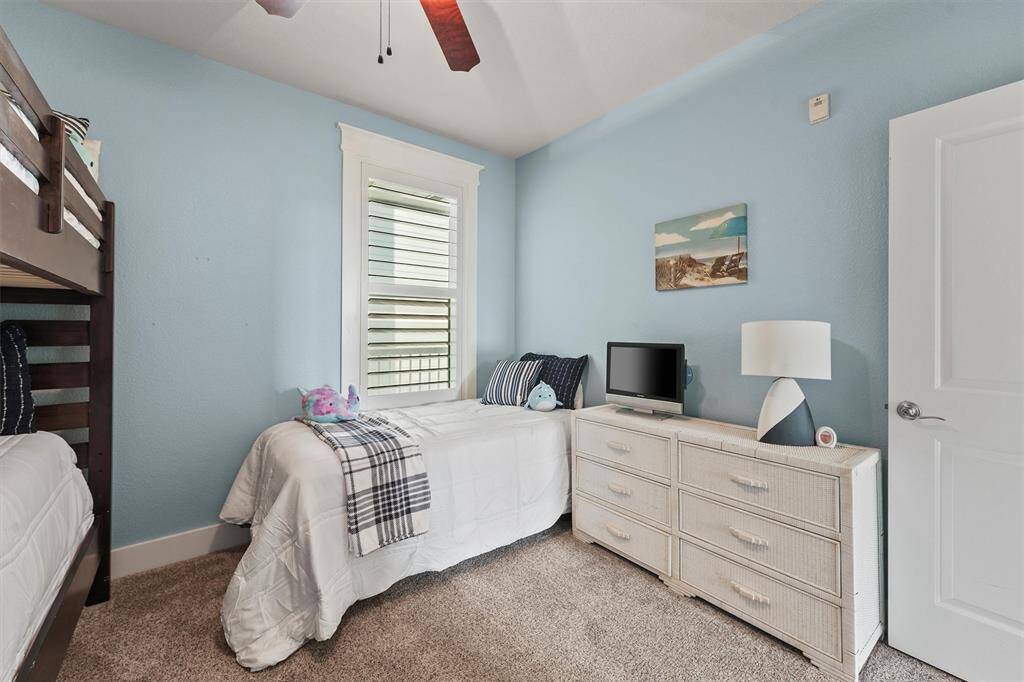 The room is equipped with a light wicker dresser and a small TV, perfect for relaxation. The blue coastal decor and ample natural light from the window enhance the room’s warm and inviting atmosphere.