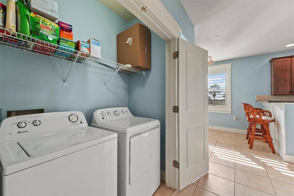This bright and functional utility room offers a convenient space with a washer, dryer, and overhead shelving for all your laundry essentials, keeping everything within easy reach.