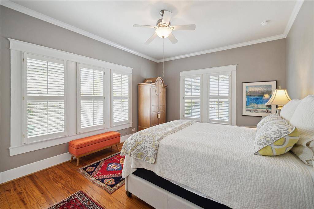 The beautiful primary bedroom is bathed in natural light, thanks to its abundance of windows.The gleaming hardwood floors, plantation shutters and ceiling fan.