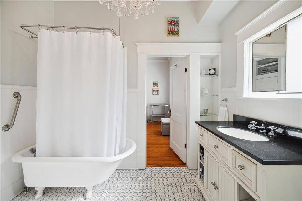 The lovely bathroom showcases a granite countertop vanity, charming white tile floors, glass shelving and a stunning clawfoot tub/shower that adds timeless character to the space.