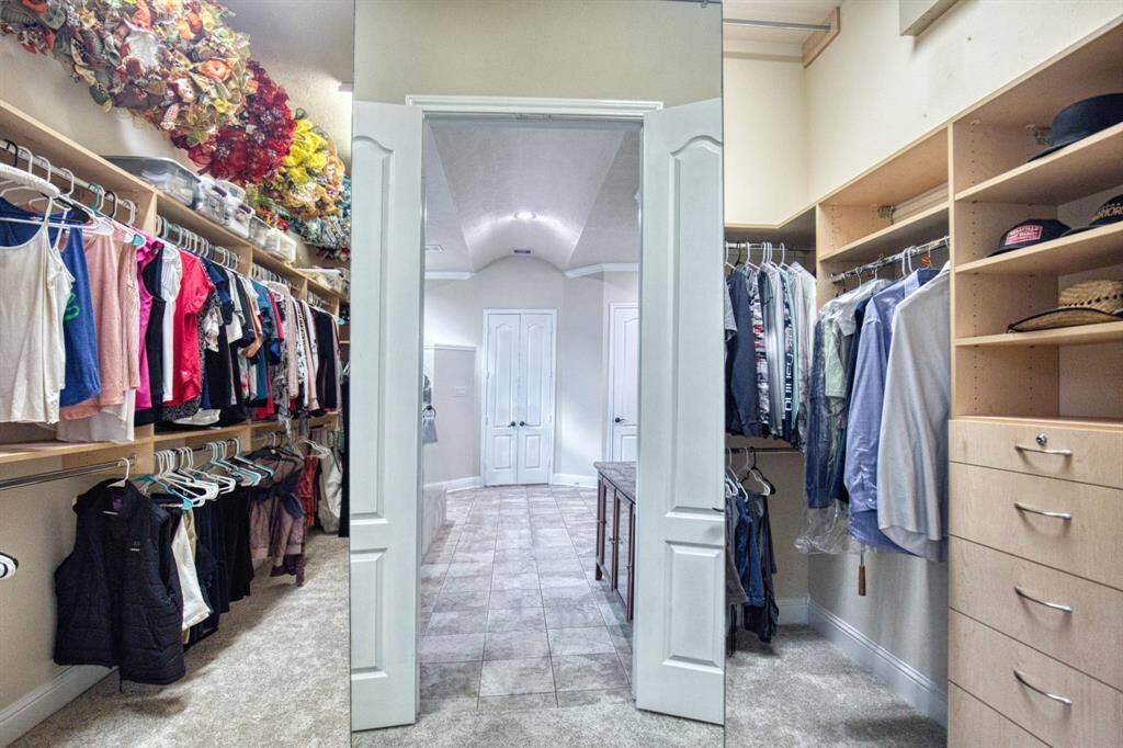 The primary bedroom features a generously-sized walk-in closet accessed through double doors, complete with a full-length fashion mirror. Designed with a split plan, it offers dedicated space for each spouse, including individual sets of drawers. The high ceilings accommodate three rows of hanging space, ensuring ample storage and organization capabilities.
