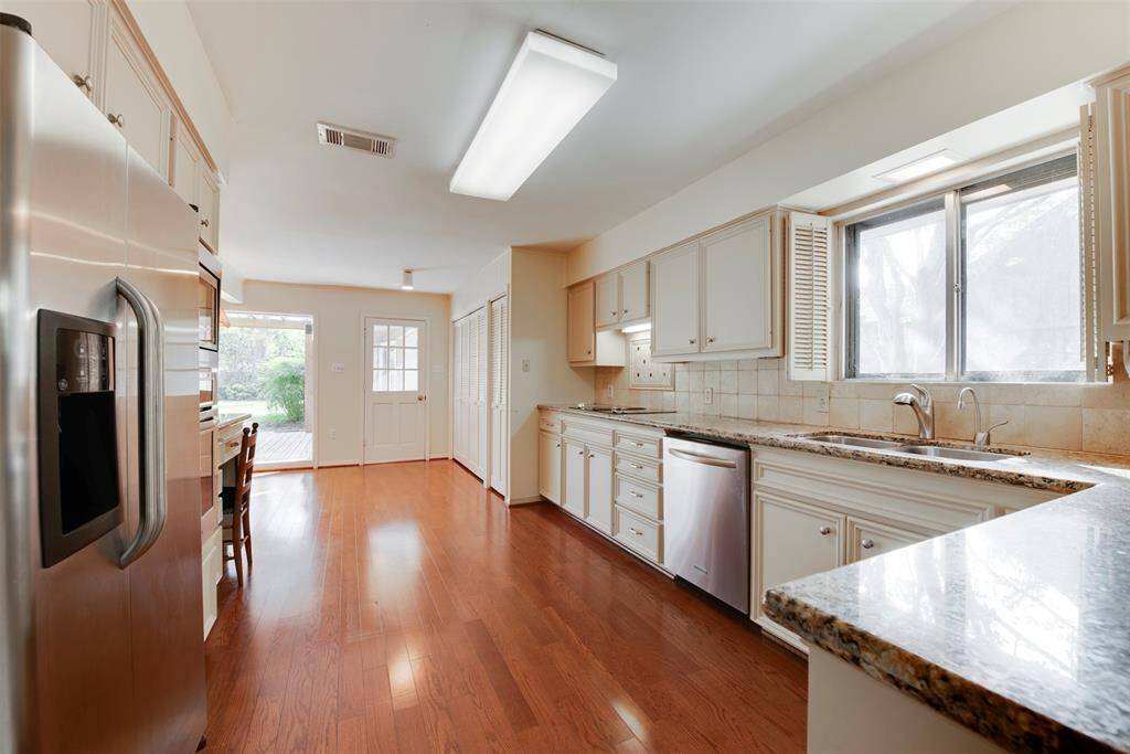 This is a bright and spacious kitchen featuring stainless steel appliances, ample cabinetry, granite countertops, and a hardwood floor. It includes a cozy dining nook and has access to an outdoor space through a glass door.