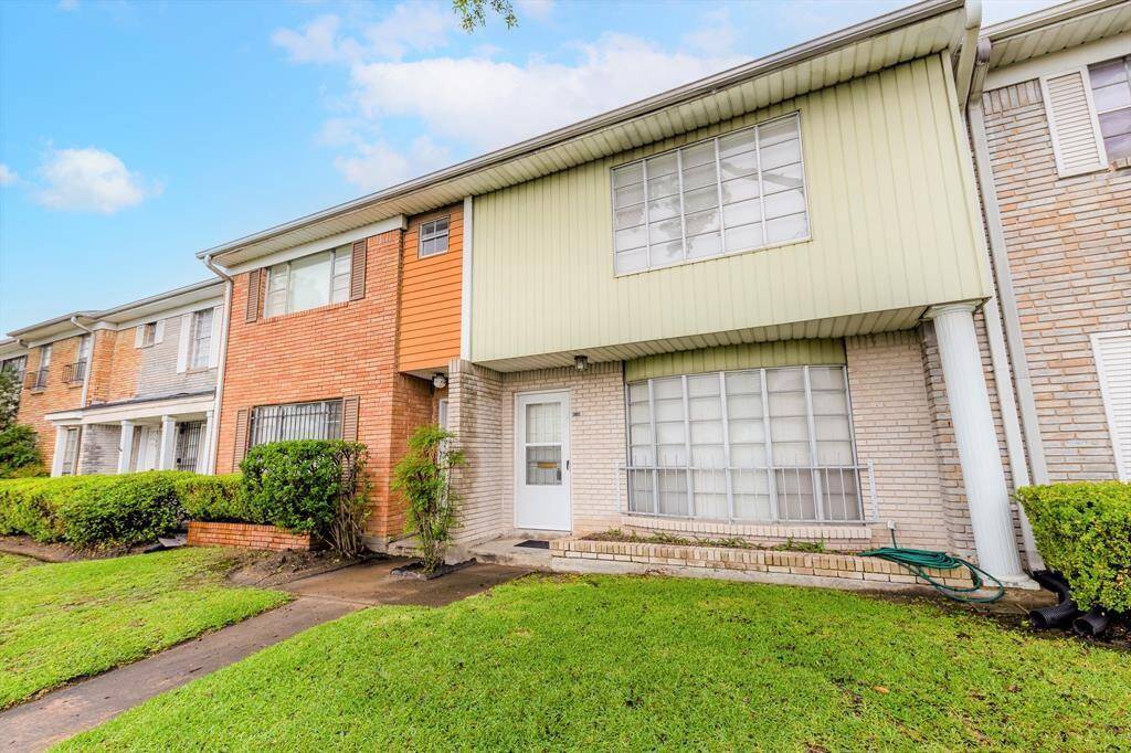 This is a two-story townhouse with a mix of brick and siding exterior. It features large windows and a small front yard with a walkway leading to the entrance.