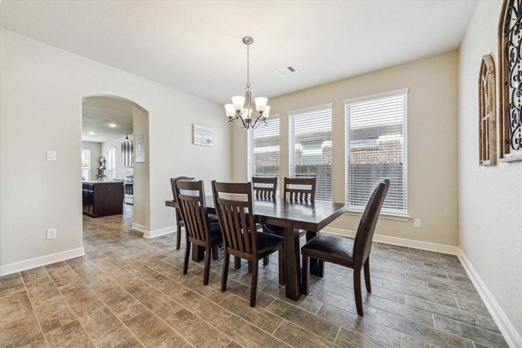 Bright dining area with large windows, a modern chandelier, and tile flooring. The space is open and leads to a kitchen, providing a seamless flow for entertaining.