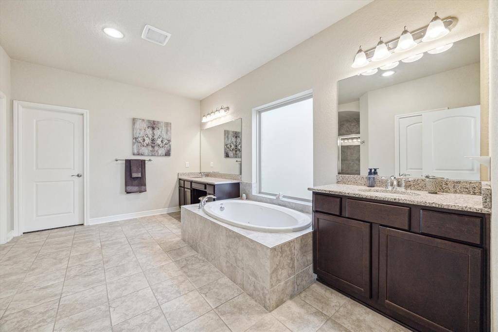 Spacious bathroom with a large soaking tub, dual sinks with granite countertops, and ample storage. Neutral tones and tile flooring create a modern, clean look. Ideal for relaxation and functionality.