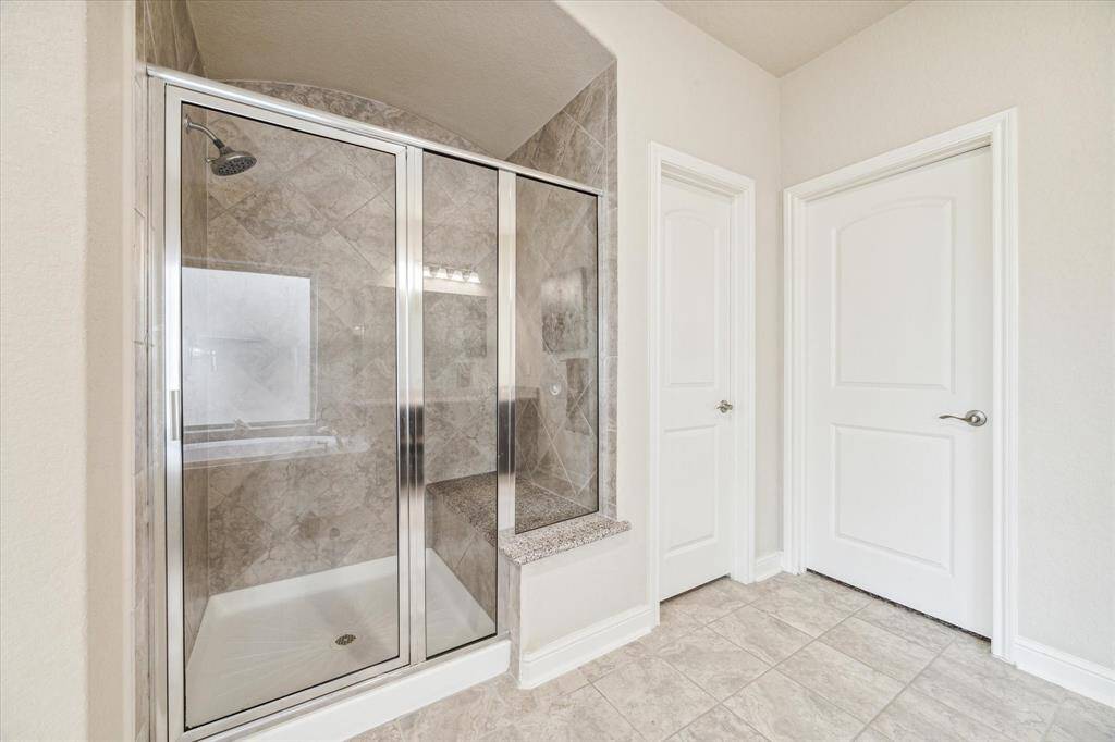 This bathroom features a spacious, modern walk-in shower with glass doors and elegant tile work. It includes a built-in bench and bright, neutral walls, creating a clean and inviting spa feel.