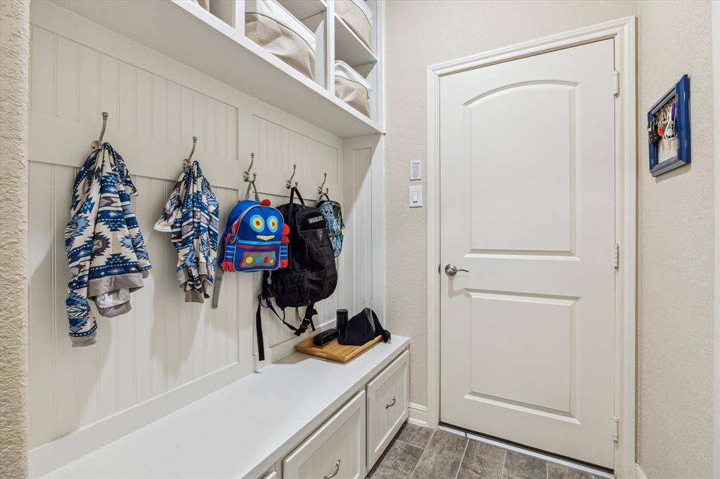 This tidy mudroom with built-in storage is located right off the garage. There are hooks for hanging jackets and bags, upper shelves for extra storage, and a bench with drawers below. The space is well-organized and practical for everyday use.