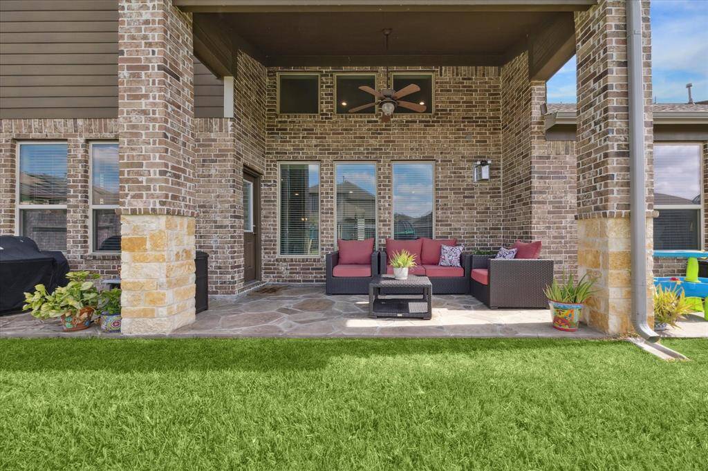 The expansive outdoor patio with a cozy seating area, surrounded by brick and stone accents. Features a ceiling fan and ample space for relaxation, overlooking a well-maintained lawn. Perfect for entertaining or enjoying quiet evenings.