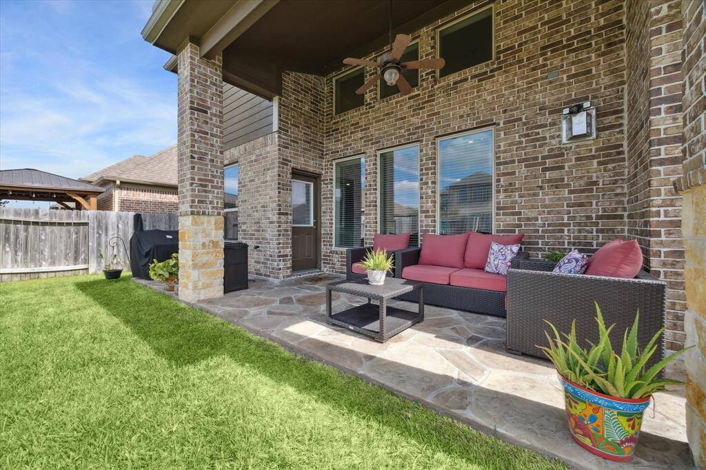 This cozy covered patio with brick walls, features a comfortable outdoor seating area. It overlooks a well-maintained lawn, providing a perfect space for relaxation and entertaining.
