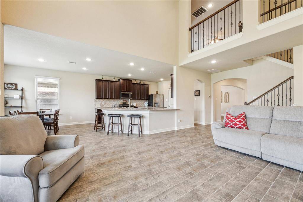 This spacious living area features an open floor plan with a view of the kitchen, high ceilings, and abundant natural light.The room also provides access to the staircase with wrought iron railings leading to the second floor.