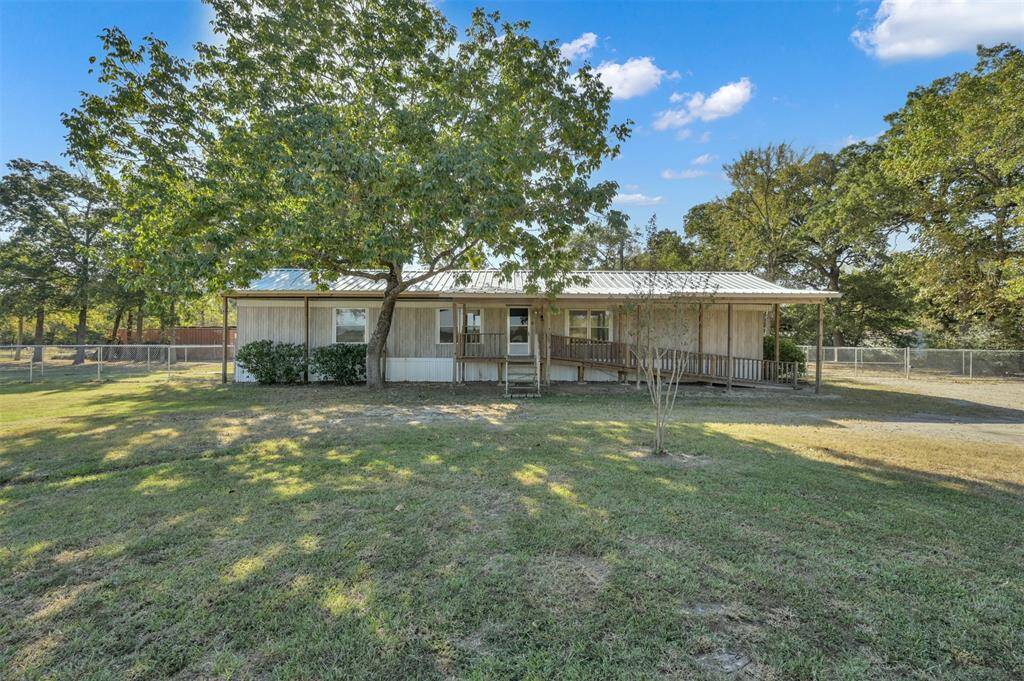 This is a single-story home featuring a spacious front yard with mature trees, a covered porch, and a fenced perimeter, offering privacy and a serene setting.