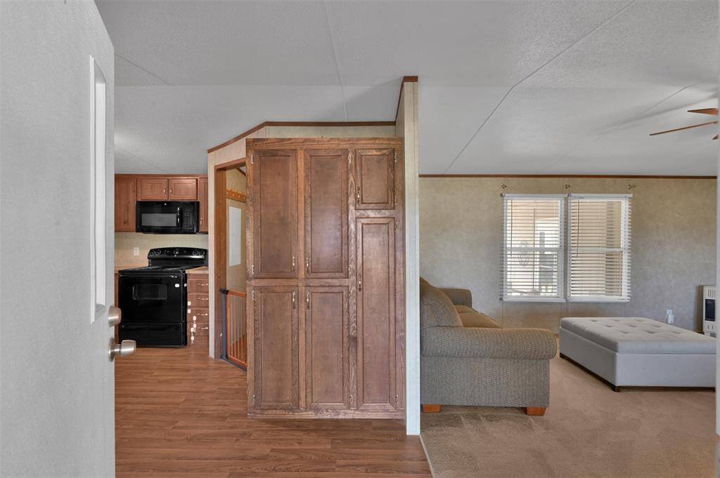 This is an open-plan living space with a seamless transition from the living area to the kitchen. It features vinyl flooring in the kitchen, carpet in the living area, modern appliances, and a neutral color scheme, offering a cozy