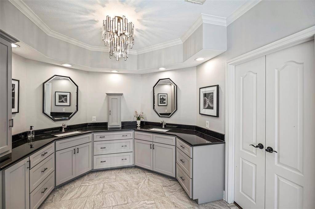 Elegantly designed primary bath with custom cabinets, granite countertops, recessed lighting, crown molding,and waterfall chandelier.