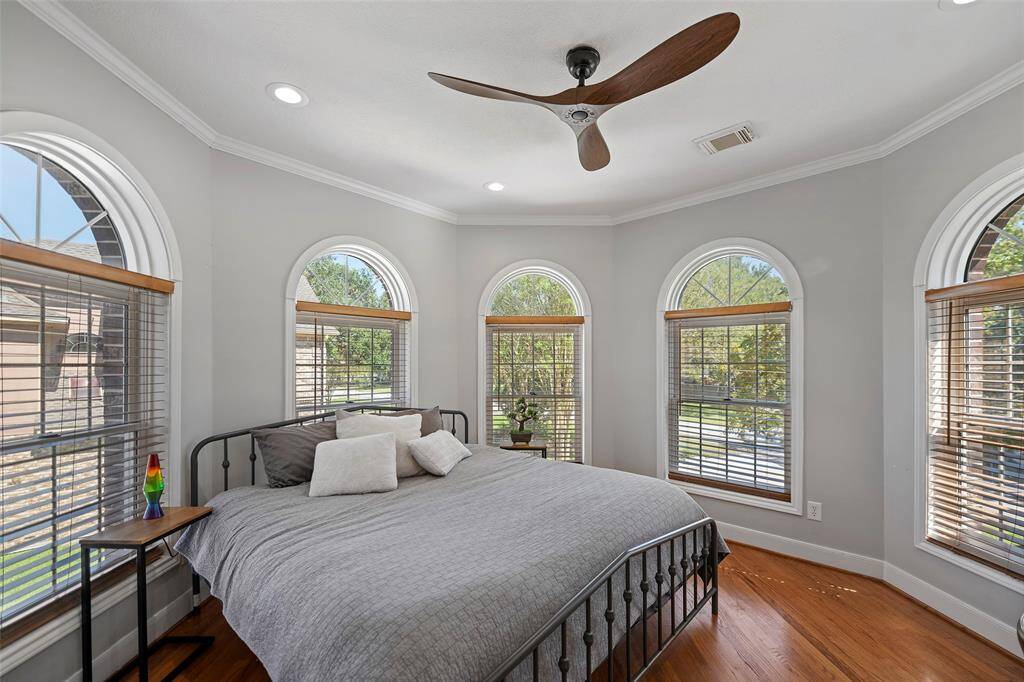 Bedroom 1, in front of the home offers plenty of natural sunlight & features hardwood floors, crown molding, recessed lighting and a wooden propeller styled ceiling fan with custom wooden window blinds.