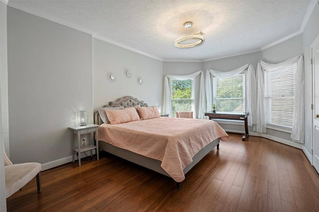 Bedroom 3 in the back of the home offers wood floors, crown molding, a modern circular ring chandelier and plenty of natural sunlight and a beautiful view of the sparkling pool out back.