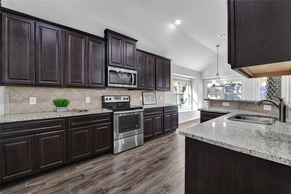 This kitchen features elegant dark cabinetry, stainless steel appliances, and granite countertops. It has a spacious layout with modern tile flooring and abundant natural light, creating an inviting and functional cooking space.