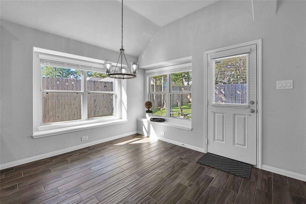 This bright room features large windows, a chic chandelier, and wood-look flooring. It opens to a backyard, offering plenty of natural light and a cozy feel.