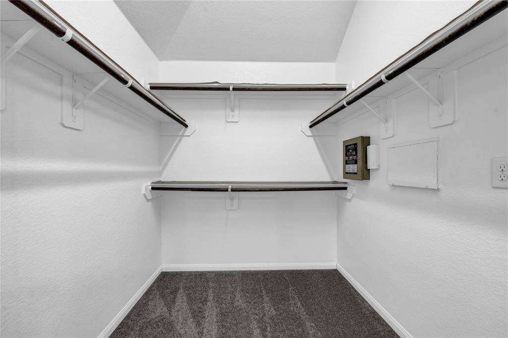 Spacious walk-in closet with multiple shelves and hanging rods, featuring clean white walls and a carpeted floor, perfect for organized storage.