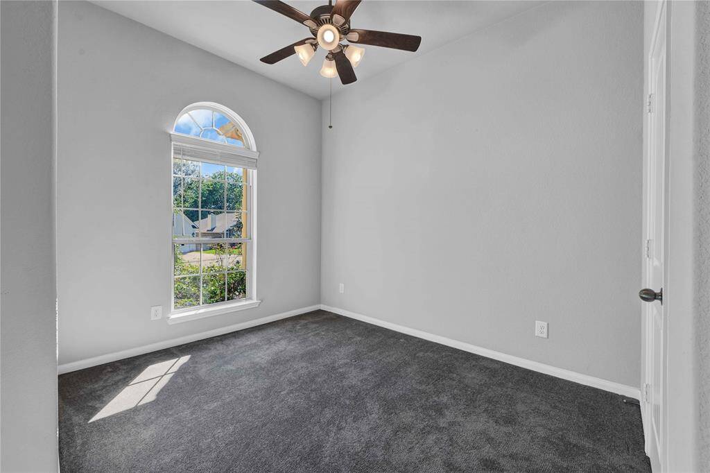 This room features a large arched window providing natural light, a ceiling fan for comfort, and neutral gray walls with matching carpet, creating a cozy and inviting space.