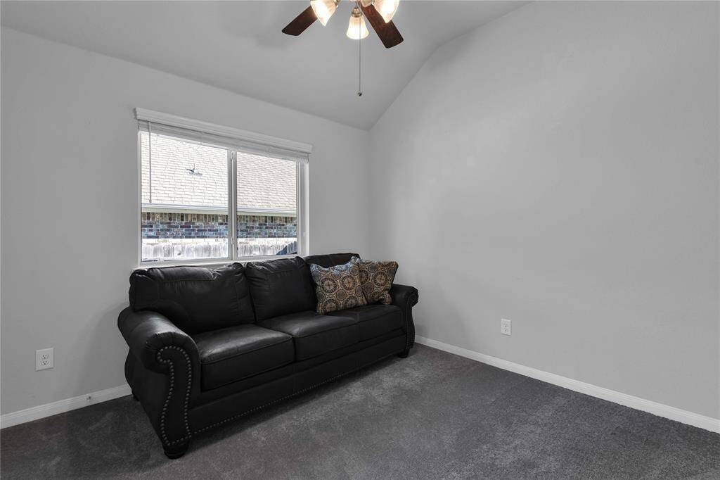 Cozy room with vaulted ceiling, featuring a black sofa and a window providing natural light. Neutral walls and carpet create a versatile space.