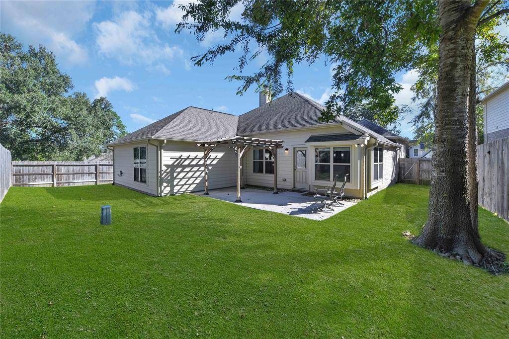Charming backyard with a spacious lawn, pergola-shaded patio, and mature trees, perfect for outdoor relaxation and entertaining.